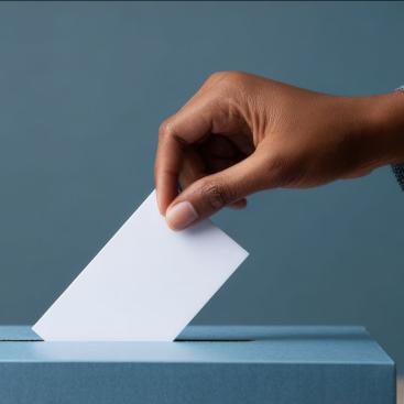hand dropping a blank ballot into a white ballot box blue background