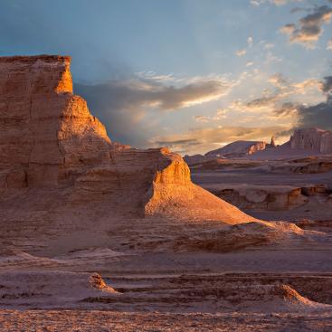 Desert landscape of ochre rock formations illuminated by golden light at sunset.