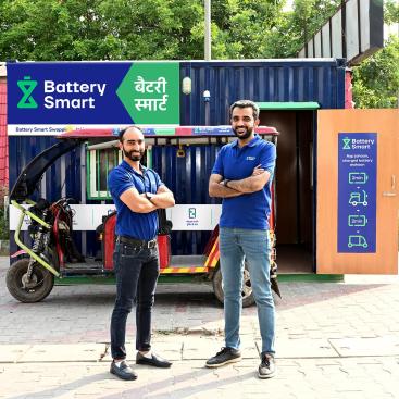 Battery Smart electric rickshaw battery swapping station with branded container and service staff standing in front