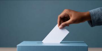 hand dropping a blank ballot into a white ballot box blue background