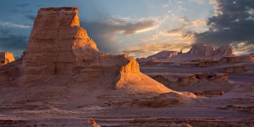 Desert landscape of ochre rock formations illuminated by golden light at sunset.