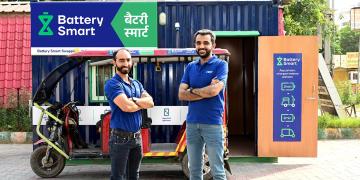 Battery Smart electric rickshaw battery swapping station with branded container and service staff standing in front
